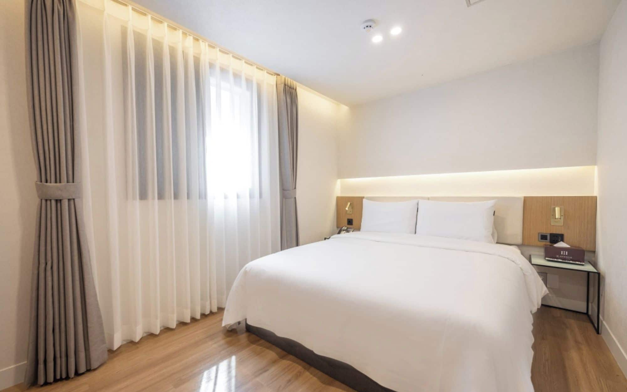 Una habitació d'hotel amb un llit gran, una taula de nit i una finestra amb cortines.