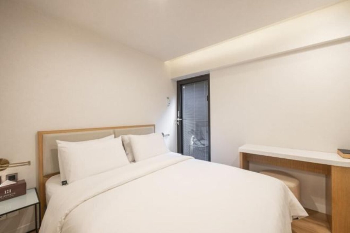 A hotel room with a bed, bedside table, and a small desk with a chair.