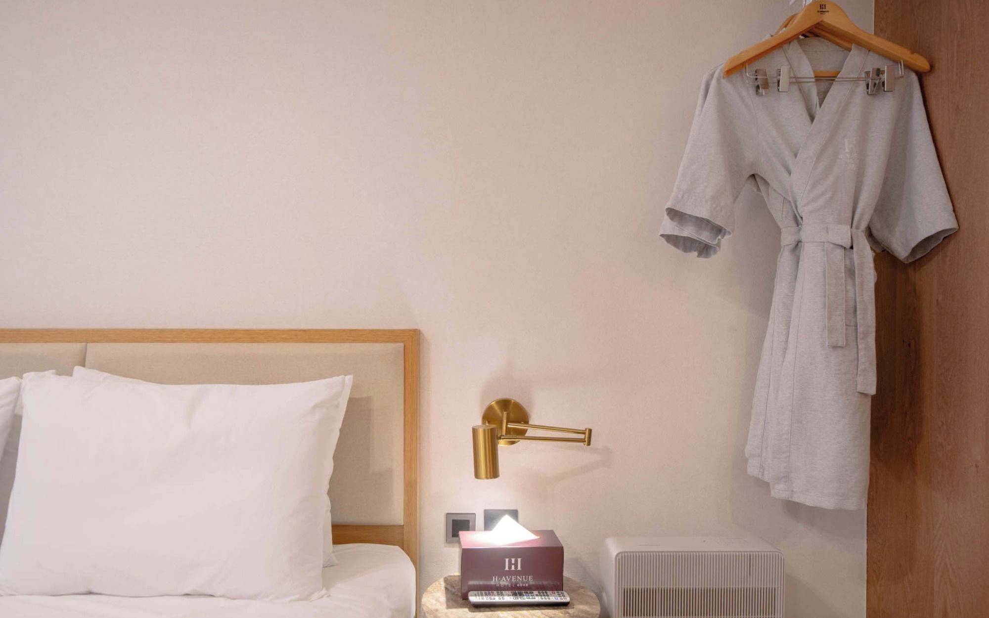A hotel room with a bed, a bedside table with a lamp, a robe hanging on a wooden hanger, and a radiator.