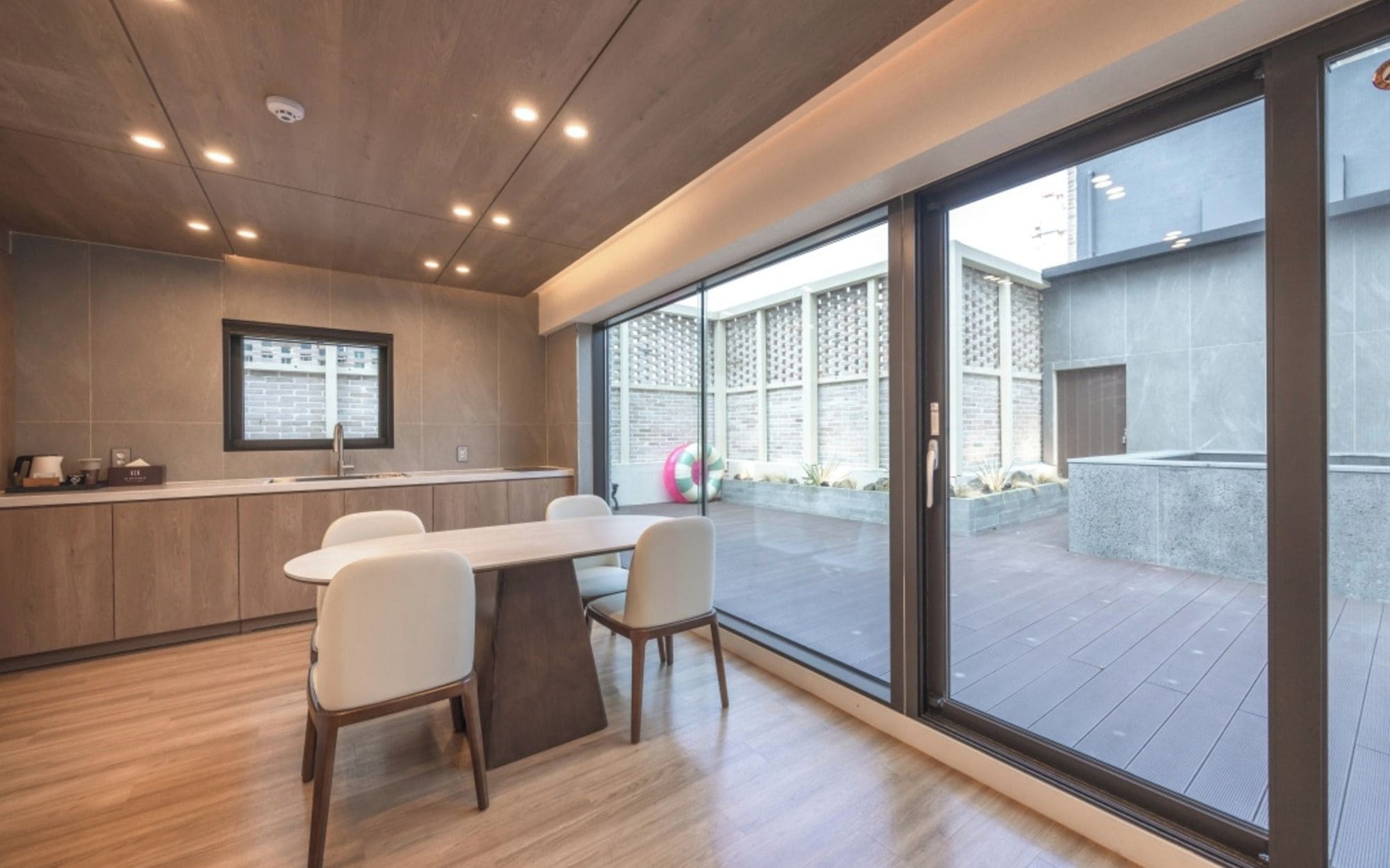 A modern kitchen with a dining area, large windows, and a view of the outside.