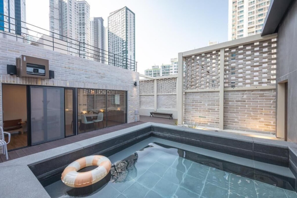 A rooftop pool area with a glass enclosure, a lounge chair, and a floating ring.