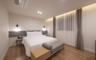 A modern hotel room with a large bed, bedside tables, a bench, and a window with curtains.