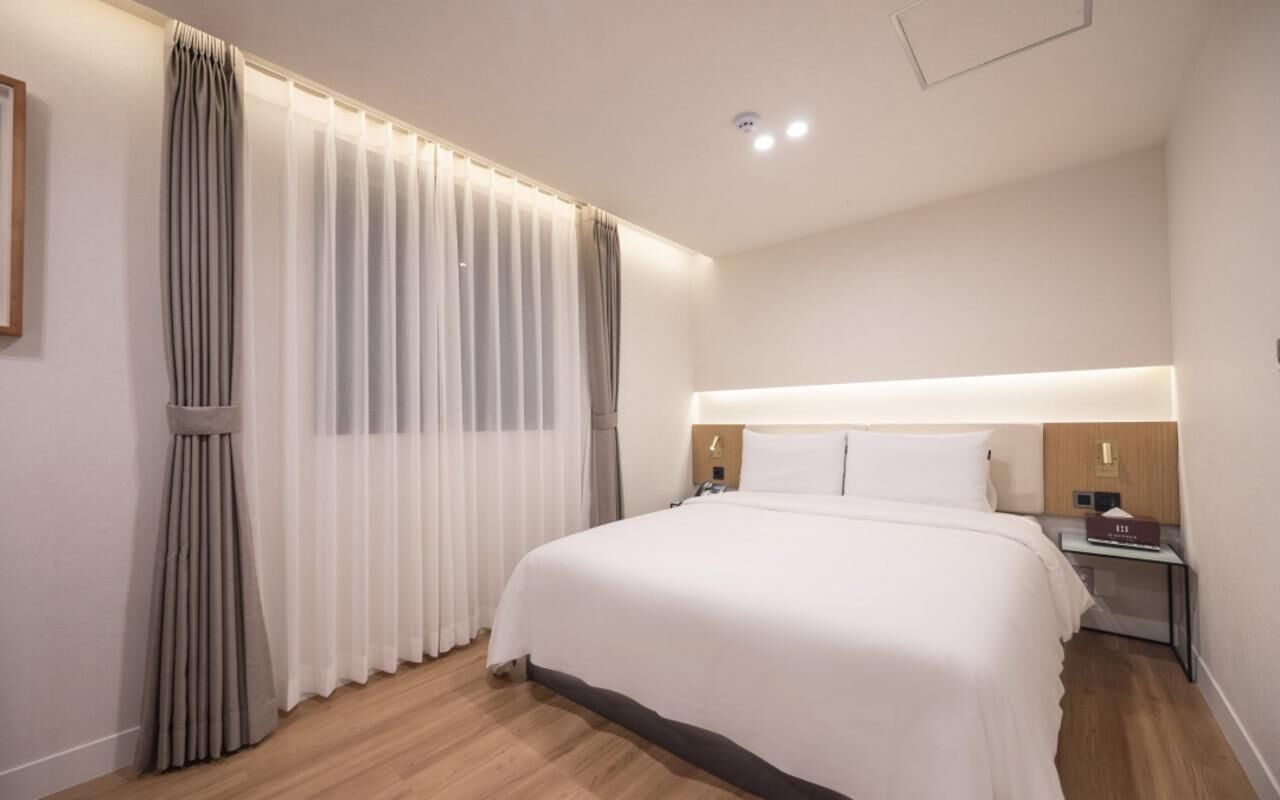 A hotel room with a large bed, a bedside table, a nightstand, and a wall-mounted light fixture.