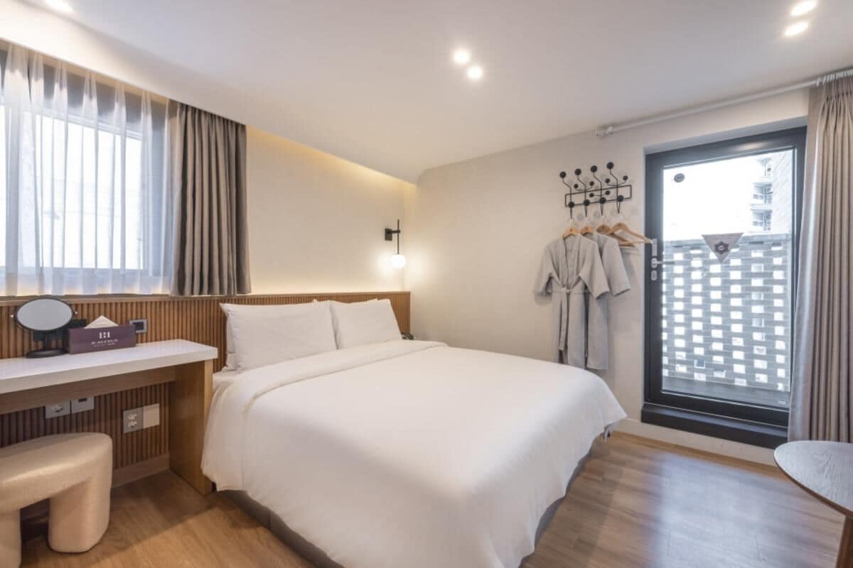 A hotel room with a bed, a desk with a chair, a vanity, and a window with curtains.