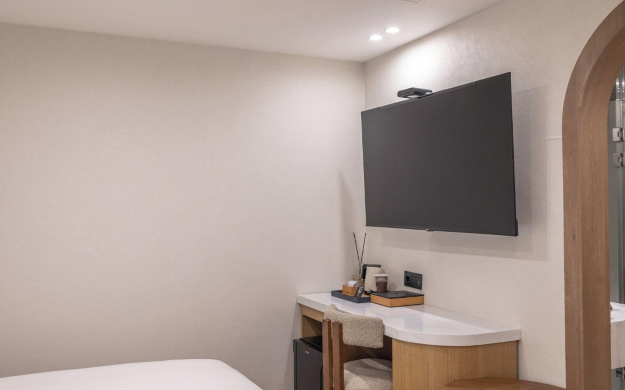 A modern bathroom with a white sink, a mirror, and a flat-screen TV mounted on the wall.