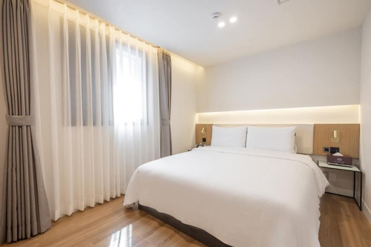 A hotel room with a large bed, a nightstand, a lamp, and a window with curtains.