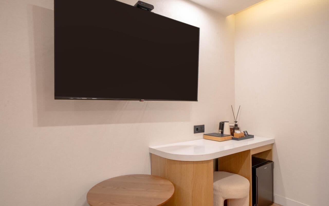 A modern bathroom with a mounted TV, a sink, a toilet, and a small wooden stool.