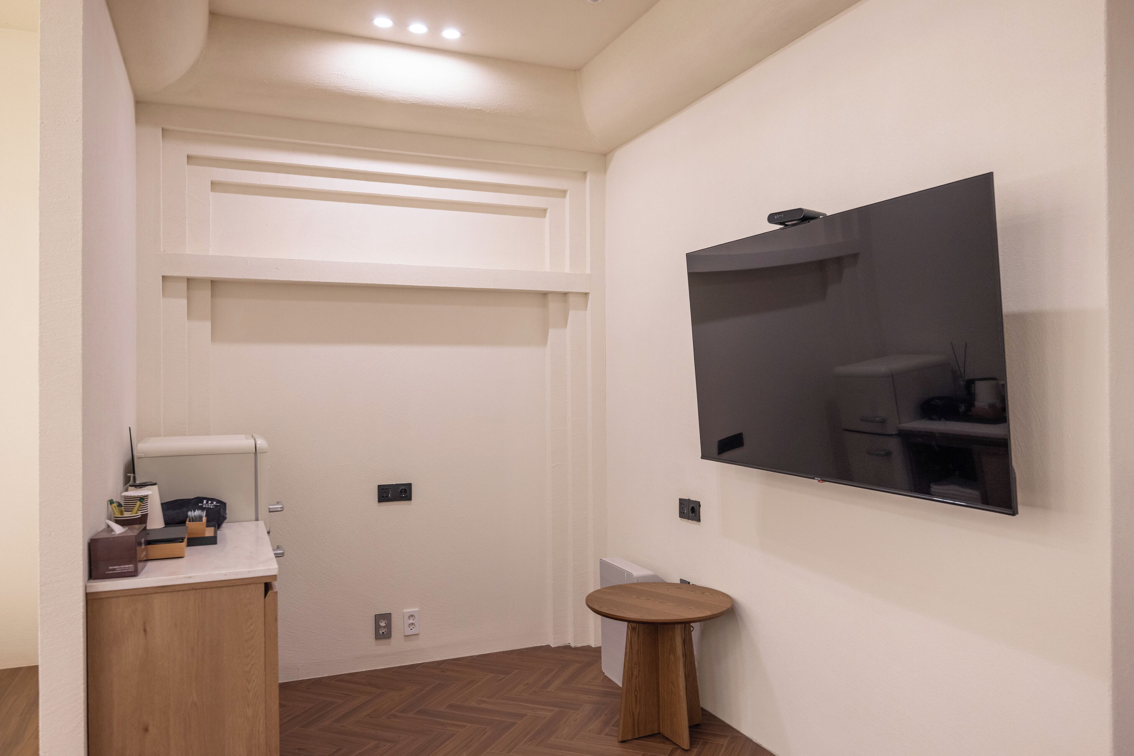 Une chambre d’hôtel moderne dotée d’un grand téléviseur à écran plat fixé au mur, d’une petite table d’appoint en bois et d’une armoire intégrée avec un miroir.