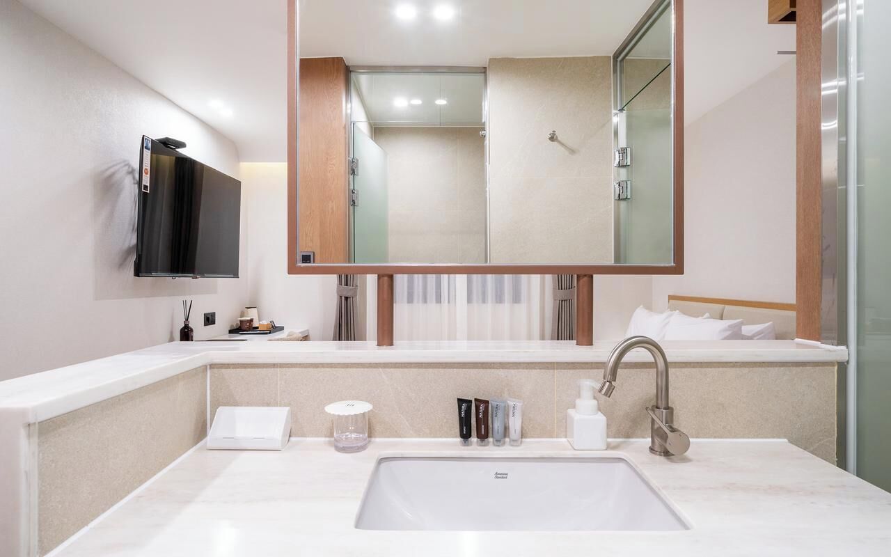 Een moderne badkamer met een grote spiegel, een inloopdouche en een wit wastafelmeubel met toiletartikelen.
