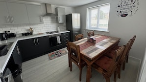 Una cocina moderna con armarios blancos, una mesa de comedor con sillas de madera y una ventana con persianas.