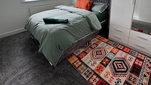 Un dormitorio con una cama, una ventana con persianas, un radiador, un armario y una alfombra estampada.