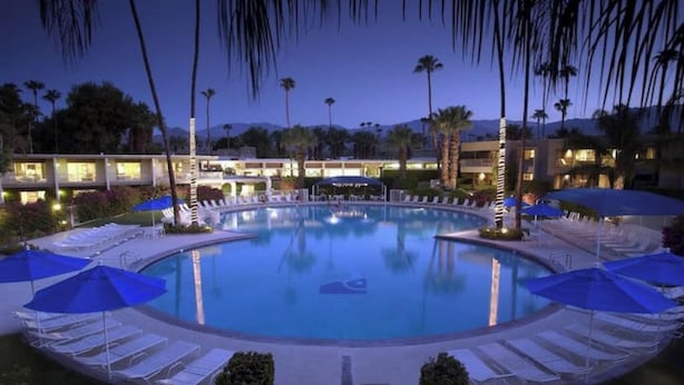A pool surrounded by lounge chairs and umbrellas, with buildings in the background. - Location, Location, Location - Shadow Mountain Resort South Palm Desert  (Palm Desert)