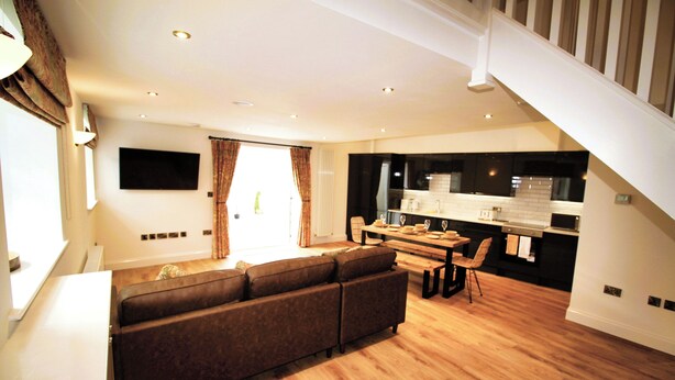 A modern living room with a large sectional sofa, a dining area with a table and chairs, and a kitchen in the background. - 1 Bed Cottage - Plus Sofa Bed - Sleeps 4 - Pets (Berwick-upon-Tweed)