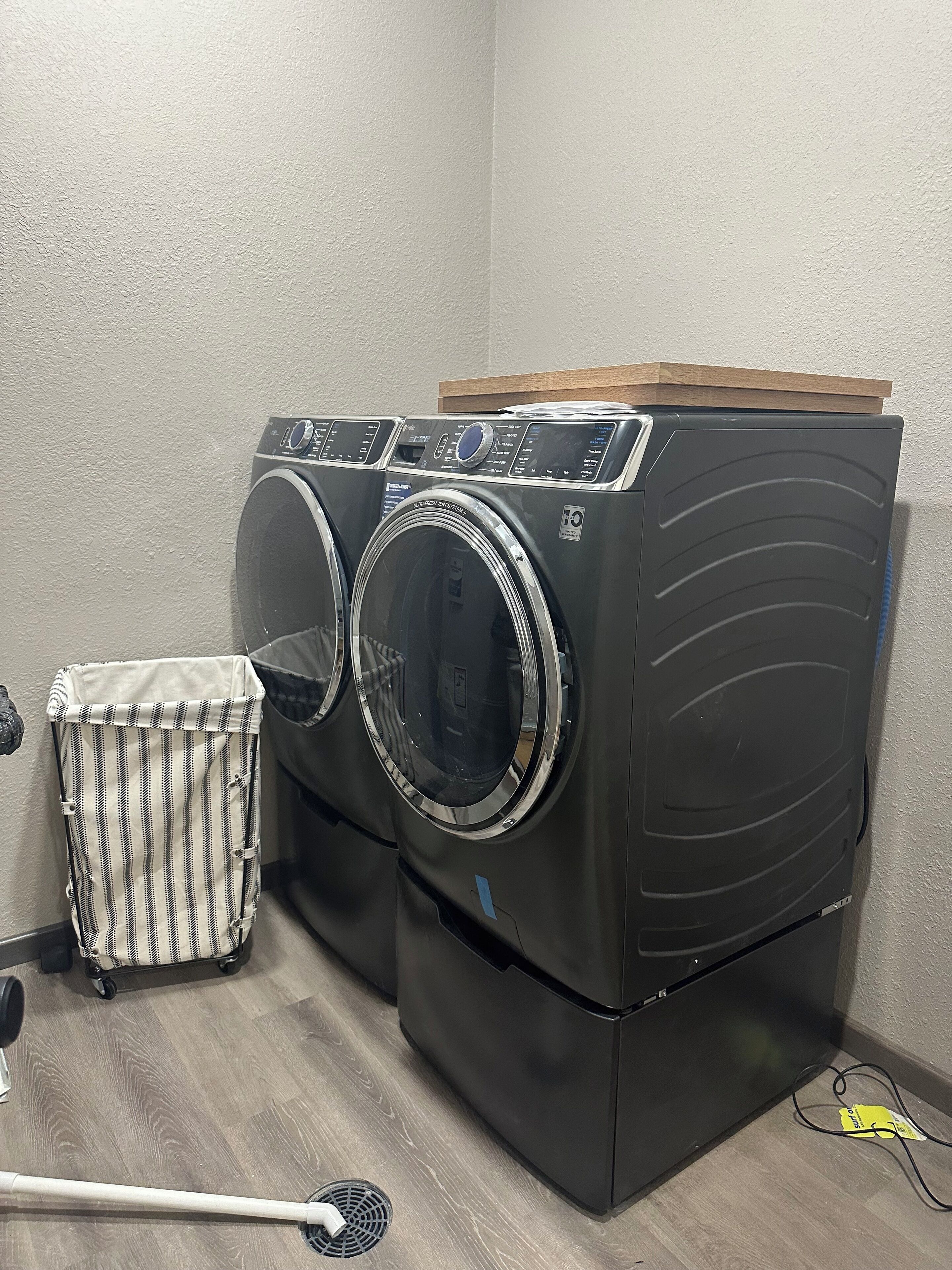 Un espace buanderie comprenant deux machines à laver à chargement frontal superposées, un panier à linge à rayures et un balai.