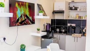 A modern kitchen with a flat-screen TV, a dining table, and a small refrigerator. - Elclassico Studio Jkia Airport View (Nairobi)