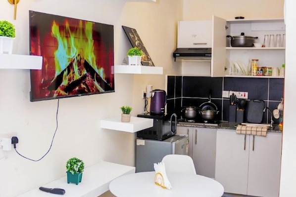 A modern kitchen with a flat-screen TV, a dining table, and a small refrigerator. - Elclassico Studio Jkia Airport View (Nairobi)