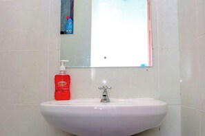 A bathroom with a white sink, a red bottle of hand soap, and a mirror above the sink. - Elclassico Studio Jkia Airport View (Nairobi)