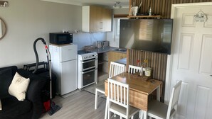 A compact kitchen with a microwave, oven, and sink. There is a dining table with chairs and a small rug. - Great Yarmouth - Chalet - Sleeps 5 - Parking (Great Yarmouth)