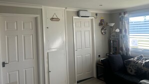 A room with white doors, a welcome sign, a ceiling fan, a bookshelf, and a window with curtains. - Great Yarmouth - Chalet - Sleeps 5 - Parking (Great Yarmouth)