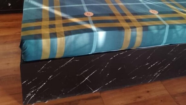 Een bed met een geruite sprei, een zwart hoofdeinde en een houten vloer.