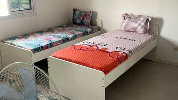 Two single beds with distinct bedding, a standing fan, and a window with a view.