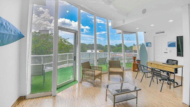 A modern room with large sliding glass doors leading to a balcony, a wooden table, and a glass coffee table. - Surfo House (Tamarindo)