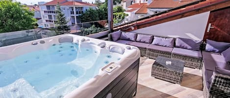Una terraza en la azotea con jacuzzi, mobiliario exterior y vistas a la ciudad.