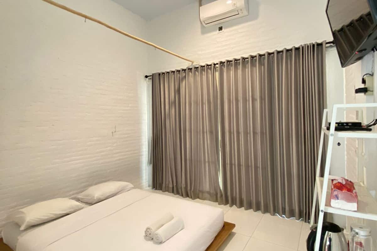 Ein Hotelzimmer mit einem Einzelbett, einem Deckenventilator, einer Klimaanlage, einem an der Wand montierten Fernseher und einem Schuhregal mit Hausschuhen.