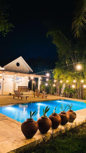 A nighttime pool area with a building, lounge chairs, and decorative lighting. - Elhoppo Pasir putih resort & resto (Sumbawa Barat)