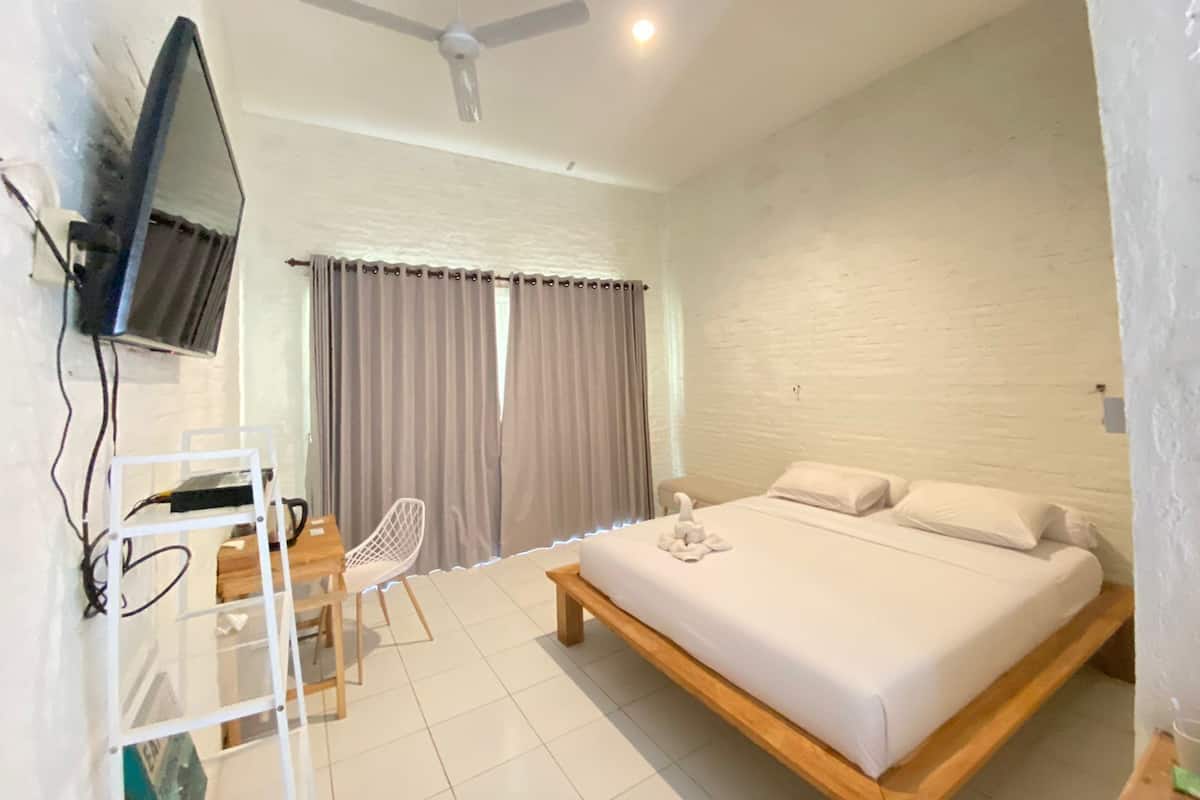 Ein Schlafzimmer mit Bett, Schreibtisch, Stuhl, Fernseher und Deckenventilator.