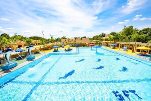 A large swimming pool with multiple lanes, surrounded by sun loungers and umbrellas, and a tropical setting with palm trees and buildings in the background. - Kabaleyan Cove Resort powered by Cocotel (San Carlos)