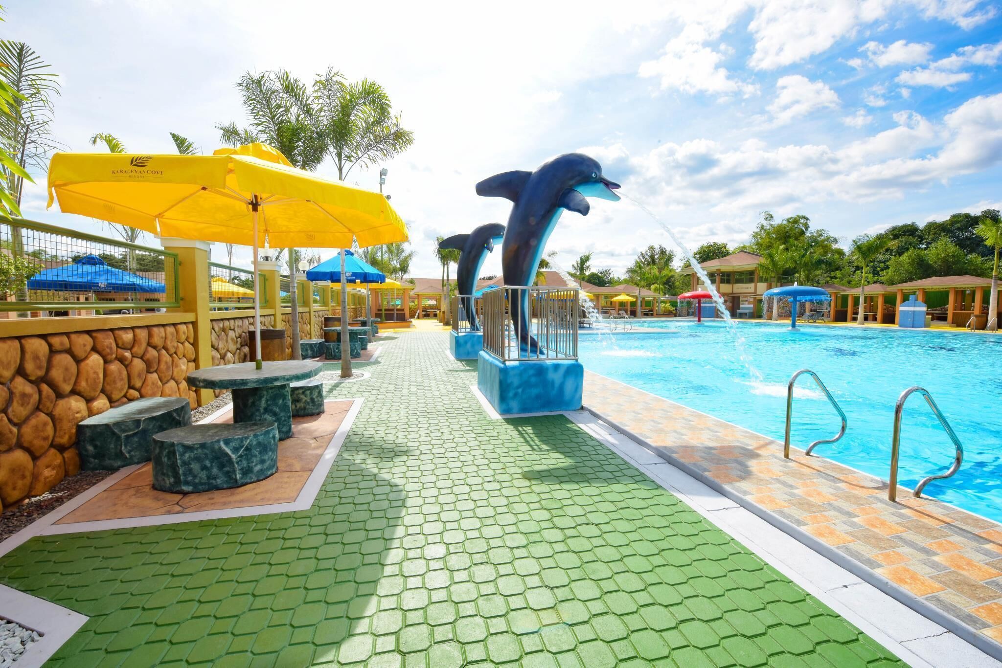 A swimming pool area with dolphin statues, umbrellas, and outdoor seating.