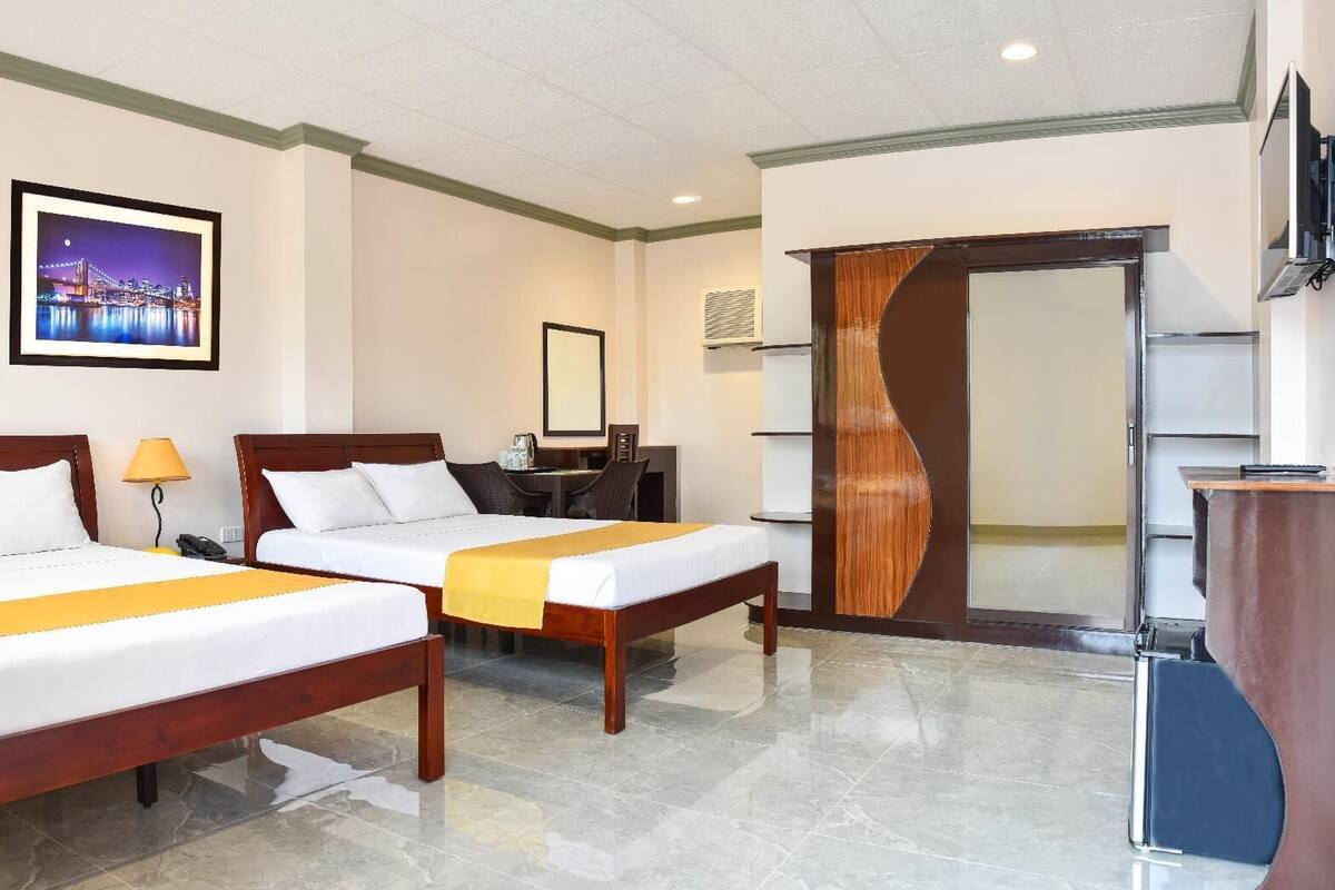A hotel room with two beds, a desk, a chair, a TV, and a framed picture on the wall.