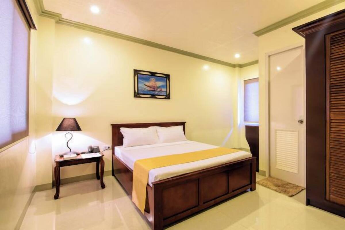 A bedroom with a bed, bedside table, lamp, and a door with a window.