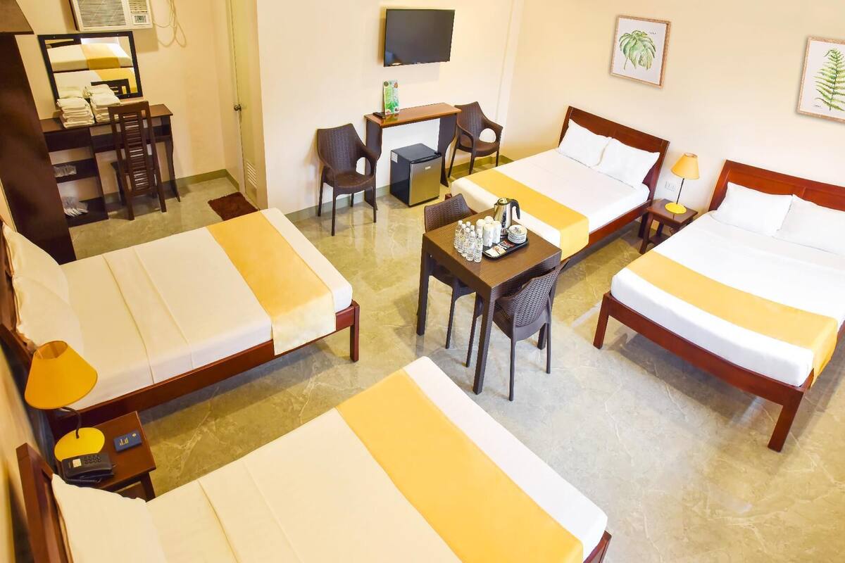 A hotel room with two beds, a desk, a chair, a TV, and artwork on the walls.