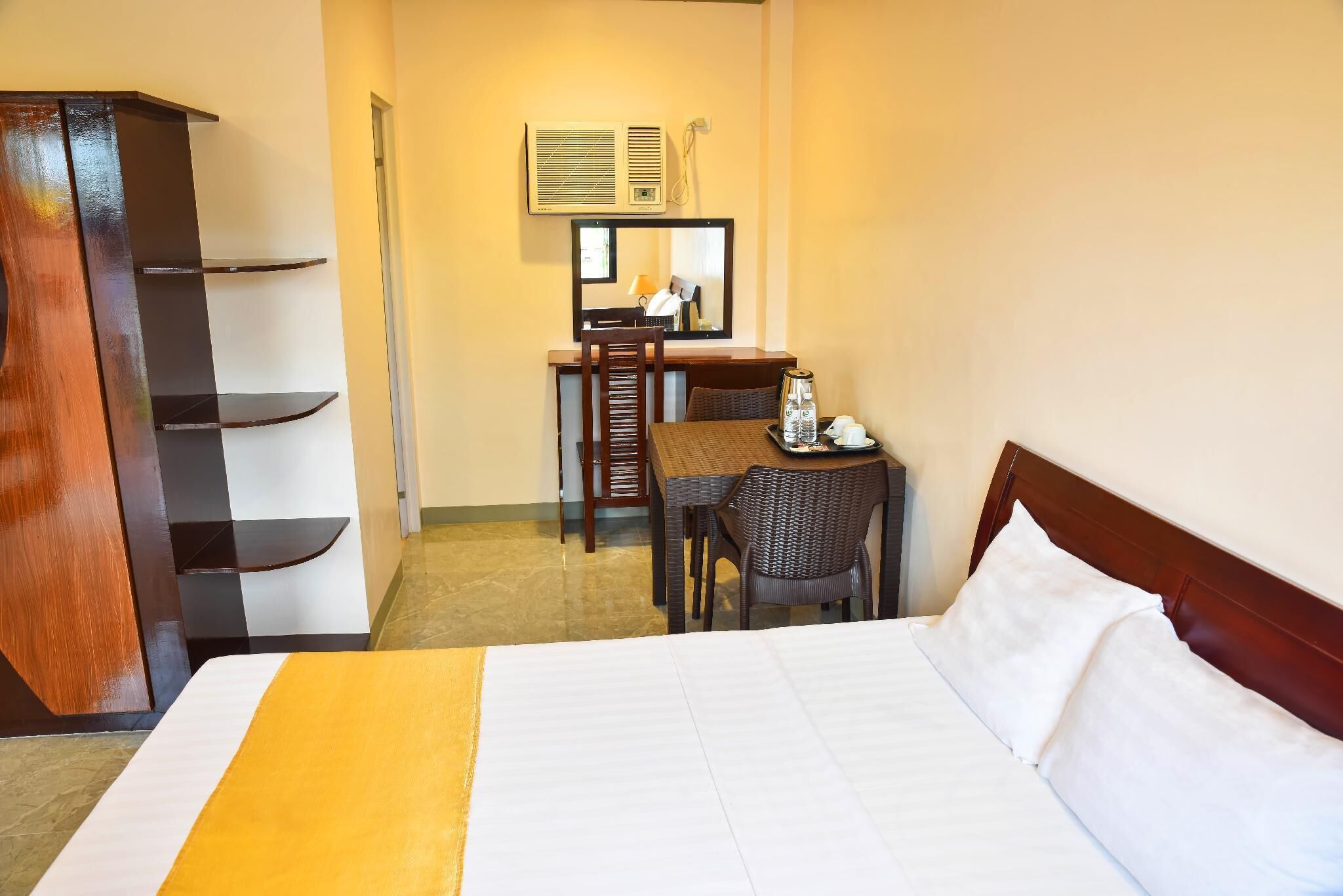 A hotel room with a bed, a desk with a chair, a wardrobe, and a mirror.