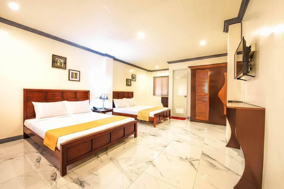 A hotel room with two beds, a TV, a desk, and a bathroom with a wooden door.
