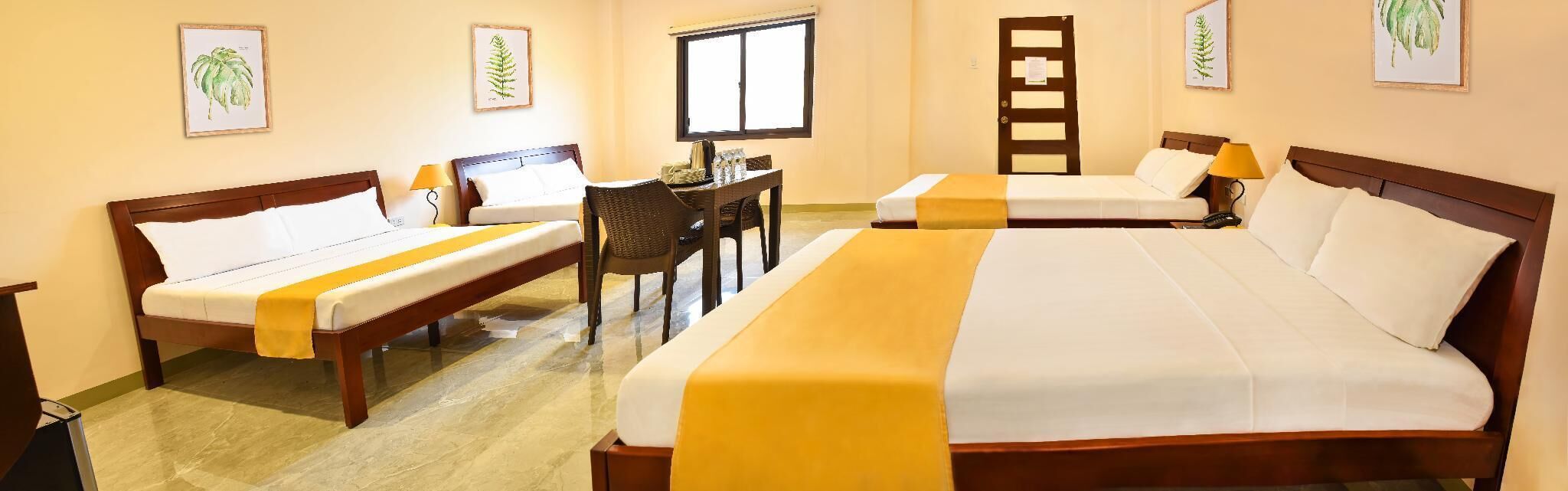 Une chambre d’hôtel avec deux lits simples et un lit double, un bureau avec une chaise et une fenêtre.