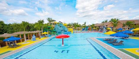 A large swimming pool with a water slide, surrounded by lounge chairs and umbrellas.