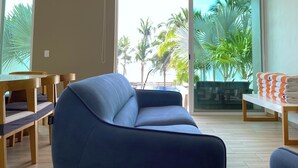 Una sala de estar moderna con un sofá azul, muebles de madera y vistas a palmeras a través de amplias ventanas.
