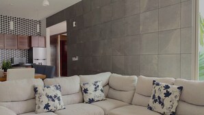 Un salon moderne avec un canapé beige, des coussins à motifs floraux et un mur orné d’un motif géométrique.
