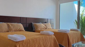 Une chambre d’hôtel avec deux lits, chacun recouvert d’une courtepointe marron matelassée et agrémenté d’oreillers assortis. Des serviettes sont posées sur les lits, et une grande fenêtre offre une vue sur la verdure environnante.