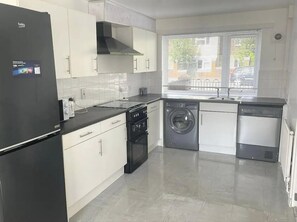 A modern kitchen with a black refrigerator, white cabinets, a stove, a washing machine, and a dishwasher. - Manchester Holiday Home (Manchester)