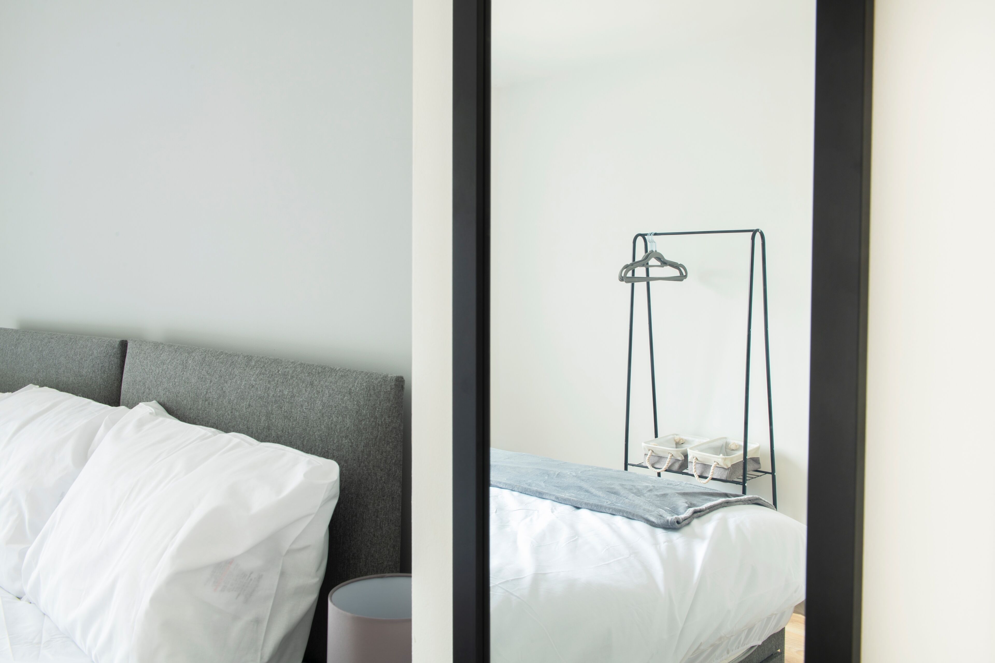 A modern bedroom with a grey headboard, a white bed, and a bedside table with a lamp.