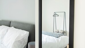 Une chambre à coucher moderne avec une tête de lit grise, un lit blanc et une table de chevet avec une lampe.