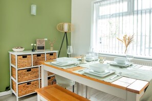 A dining area with a wooden table set for four, white plates, and a vase with dried plants.