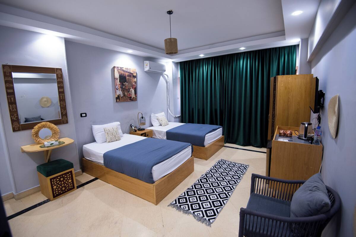 Una habitación de hotel moderna con dos camas, un escritorio pequeño, una silla, un espejo grande y una cortina verde.