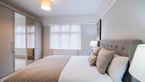 A bedroom with a large bed, a wardrobe, and a window with blinds. - Executive 4-bed house in vibrant village center

 (WALTHAM)