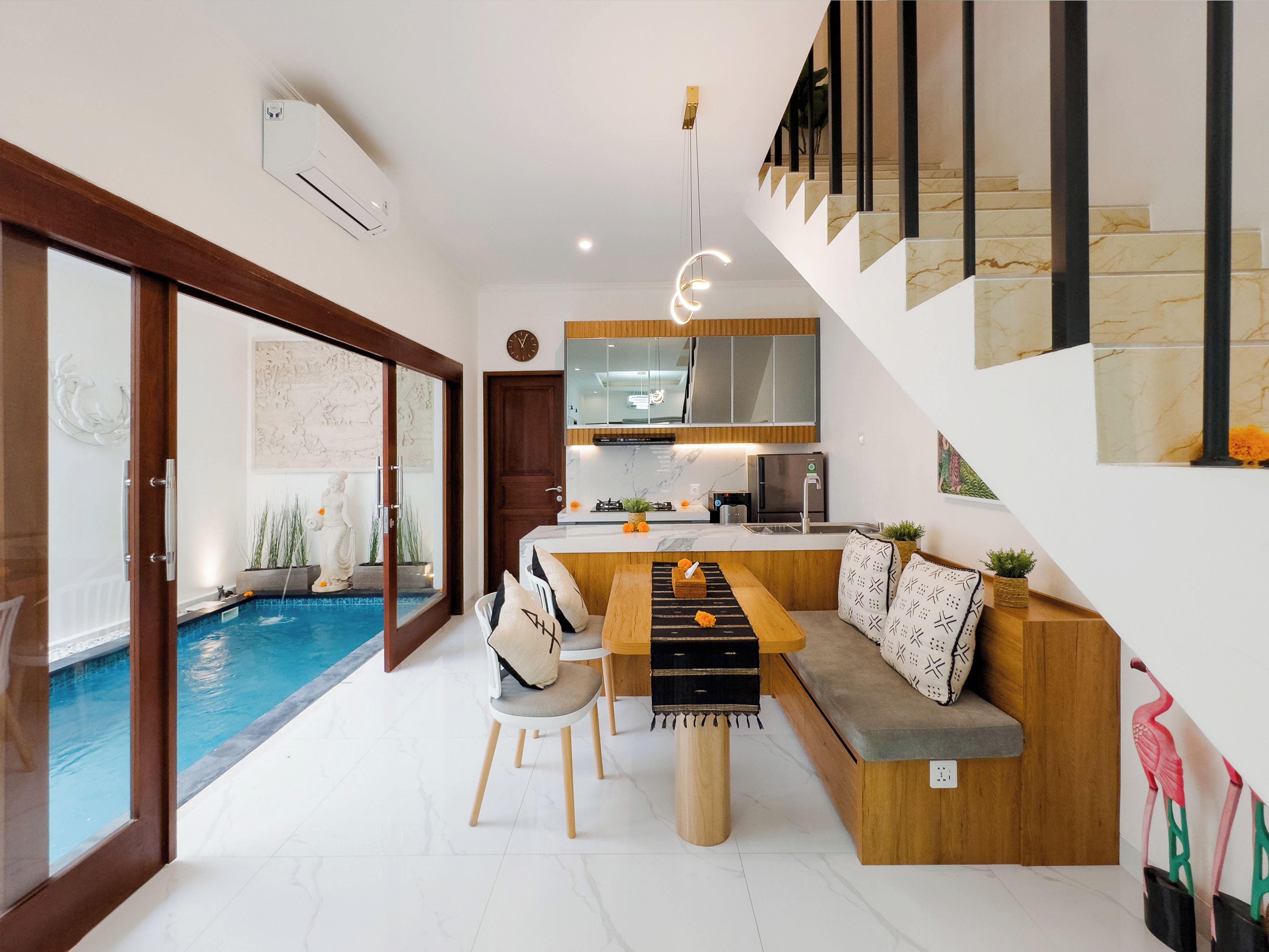 A modern kitchen with a built-in island, a dining area with a bench, and a staircase with a marble finish.