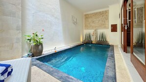 A swimming pool with a stone border, a statue, and a potted plant. - De Amelia Seminyak Villa by Nagisa Bali (Denpasar)